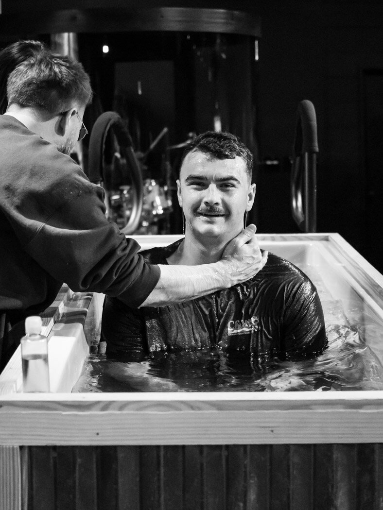 Man seated in the baptism tank as a pastor prays with him
